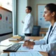 Médica analisando documentos de faturamento da clínica em frente ao computador